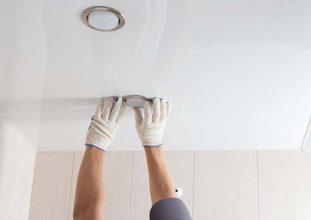 Close-up of an installer fitting a recessed light into a ceiling panel.