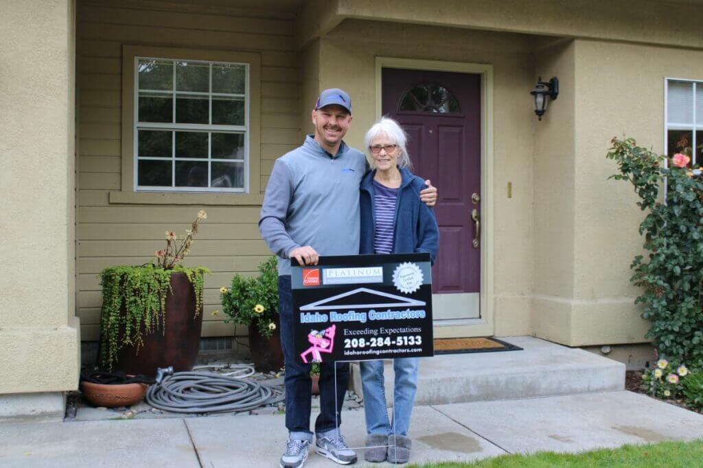 Idaho Roofing Contractors employee with a satisfied customer holding a sign that reads 'Idaho Roofing Contractors' in front of a home.