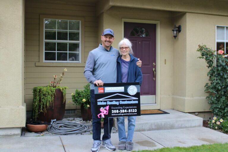 Idaho Roofing Contractors employee with a satisfied customer holding a sign that reads 'Idaho Roofing Contractors' in front of a home.