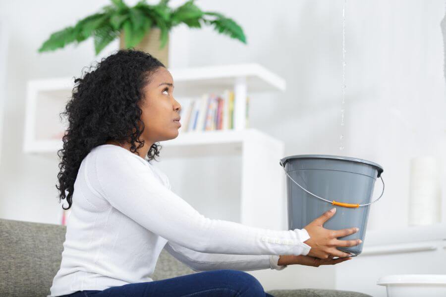 A woman holding a bucket to catch water from a ceiling leak, looking concerned.