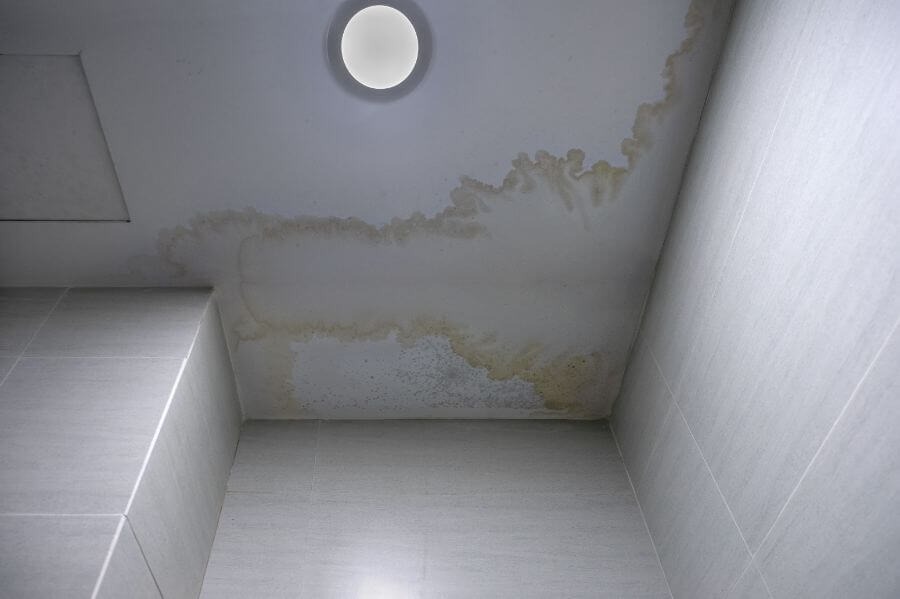 Water-damaged ceiling with extensive stains surrounding a circular recessed light fixture, indicating a leak issue.