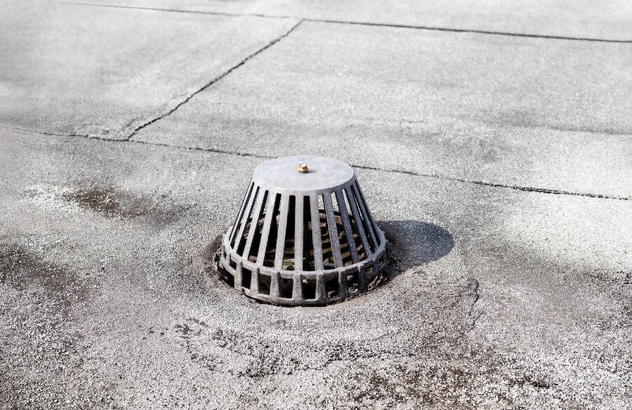 Close-up of a metal roof drain on a flat, weathered roof surface.