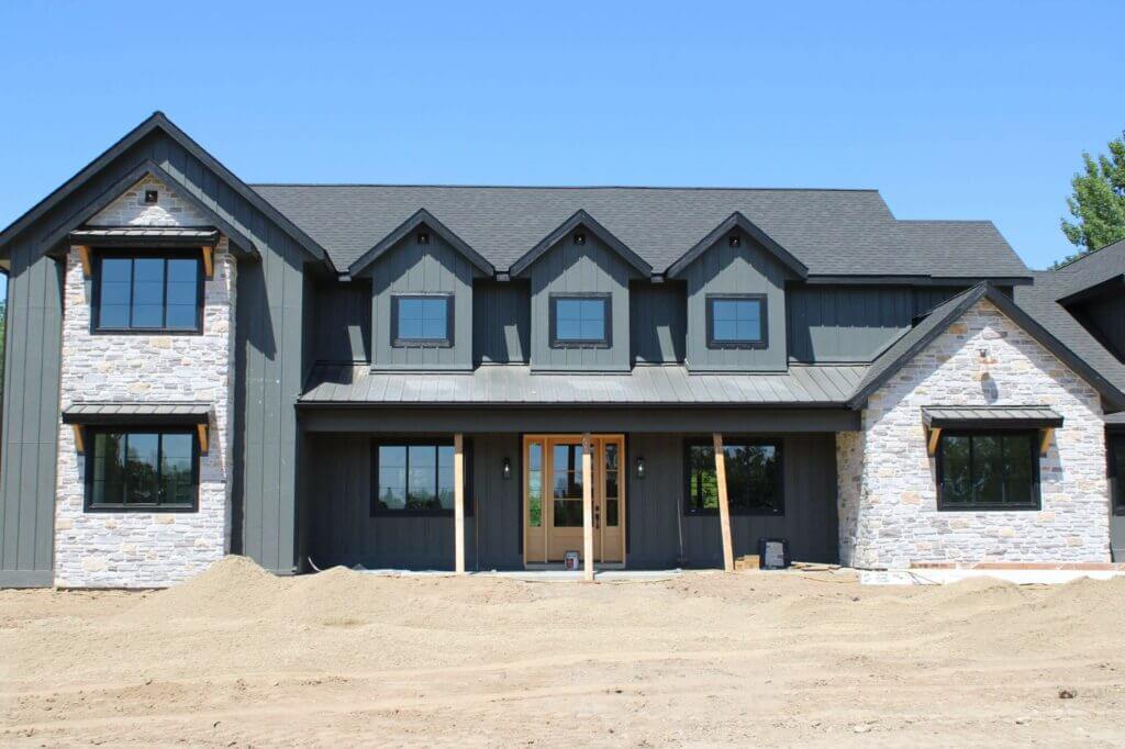 Modern dark gray house with stone accents and new roof under construction.