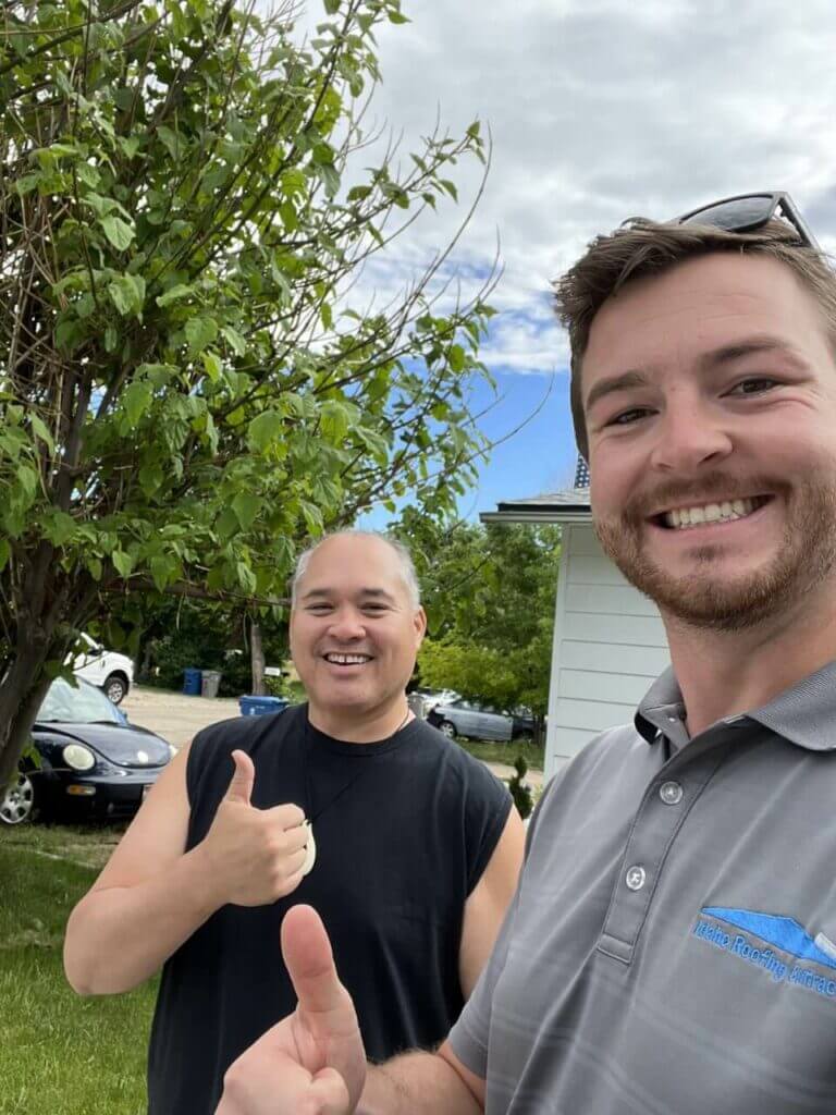 Two men smiling and giving thumbs up in front of a tree and a house.