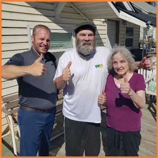 Three people standing outside a house, all giving thumbs up, smiling at the camera.