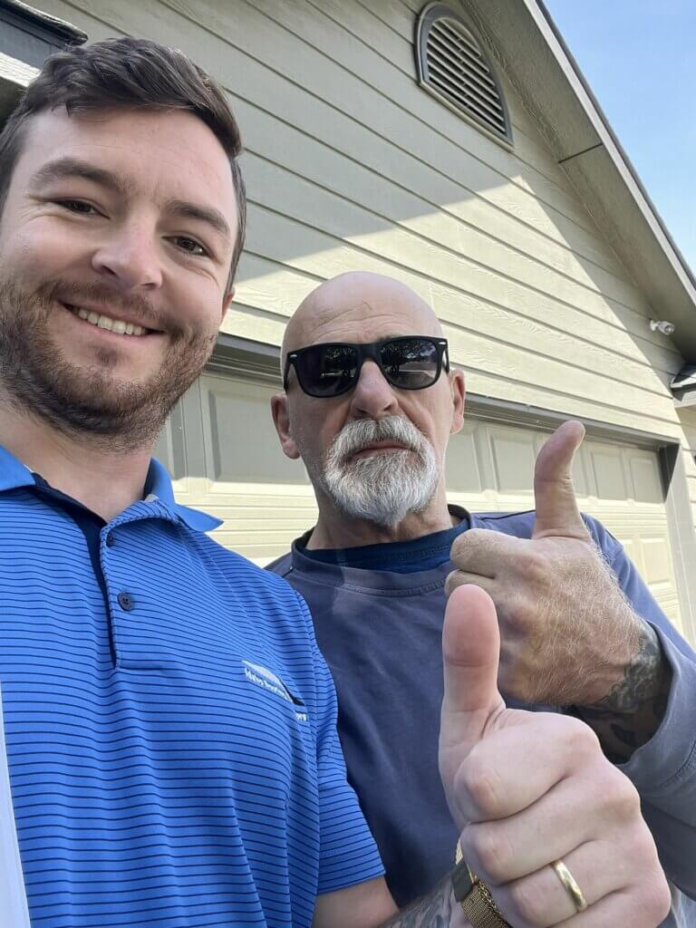 Two men standing in front of a house, both giving a thumbs-up.
