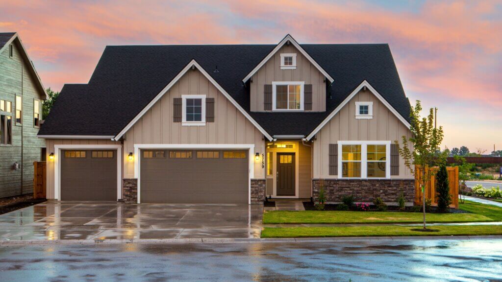 Front view of a modern house with three garage doors and a well-maintained lawn, taken at sunset