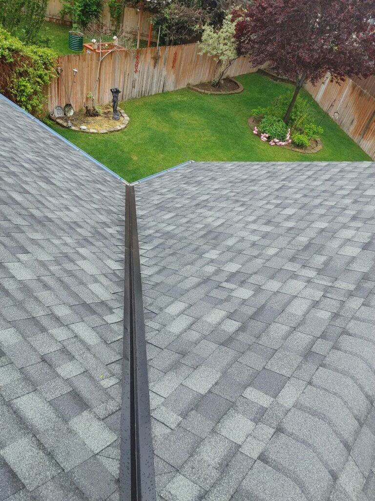 Top view of a gray shingle roof with a backyard garden and fence in the background.