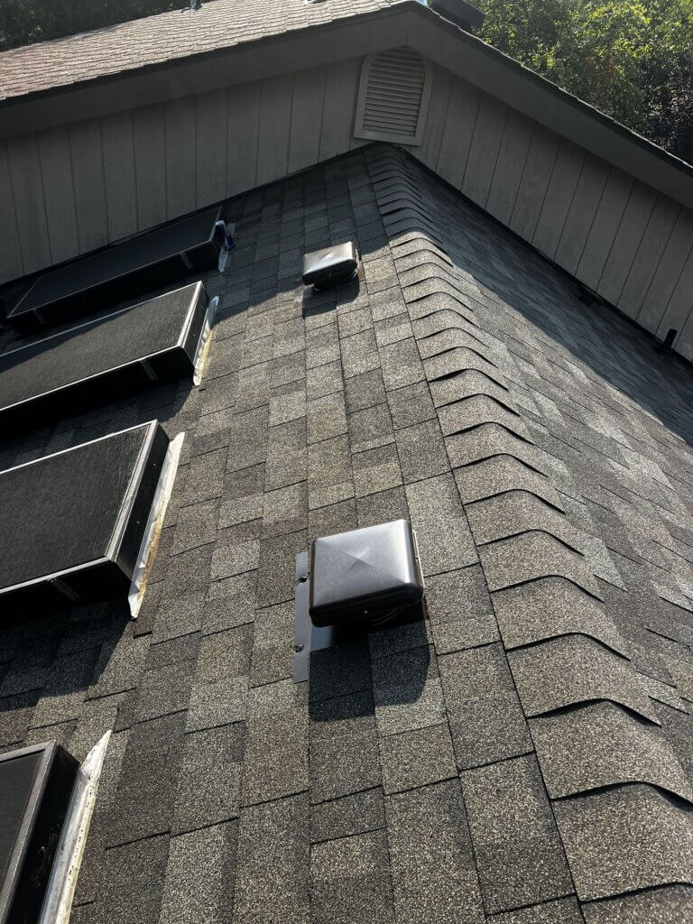 Roof replacement with three installed skylights, showcasing fresh shingles and a vent in the foreground.