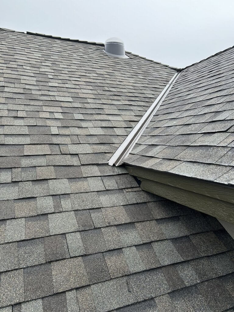 Asphalt shingle roof with white metal skylight flashing connecting different roof planes.