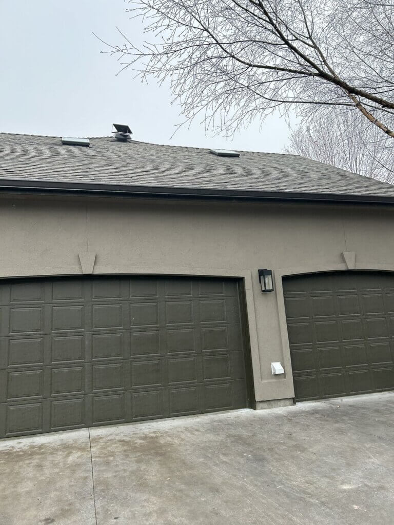 Solar roof vent on gray shingle roofing above garage doors.