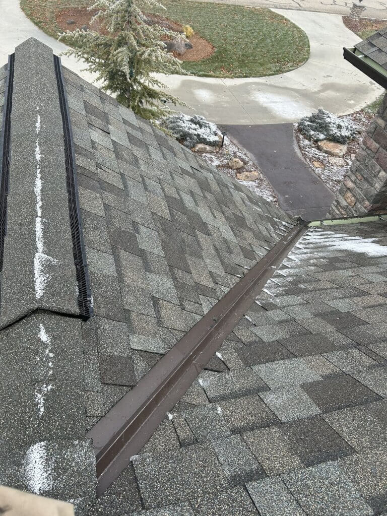 Roof valley with brown metal flashing properly installed between two sections of gray asphalt shingles.