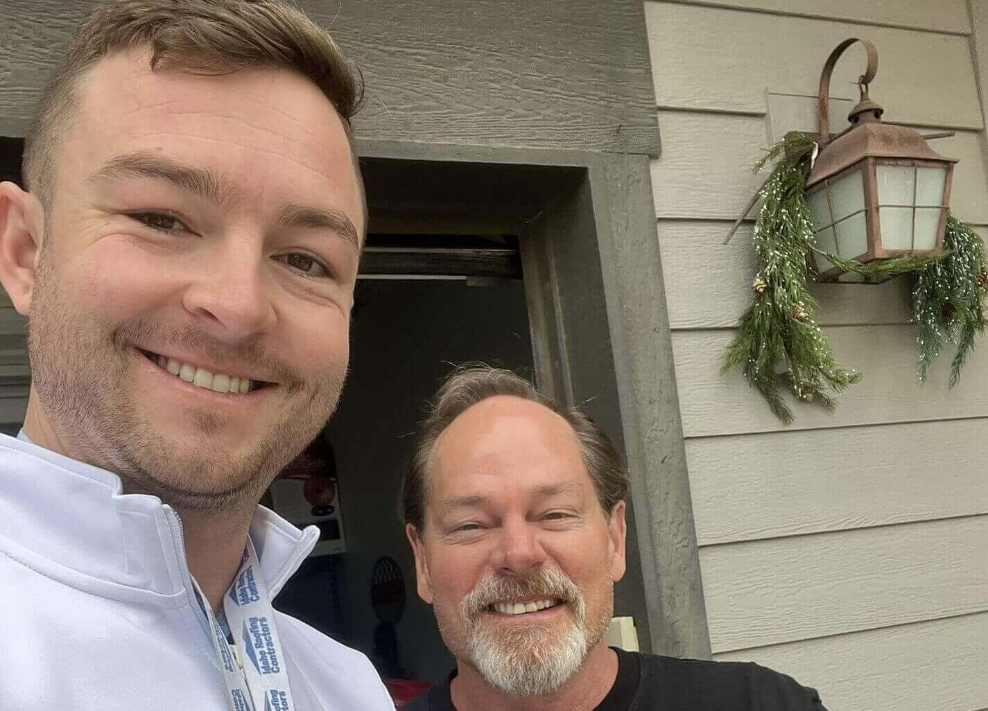 a contractor and client give each other the thumbs up outside a home that has just had roof repairs.