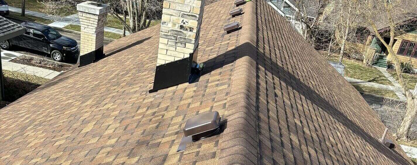Brick chimney stacks with clean flashing, several box vents, and a brown shingle roof with a ridge cap.