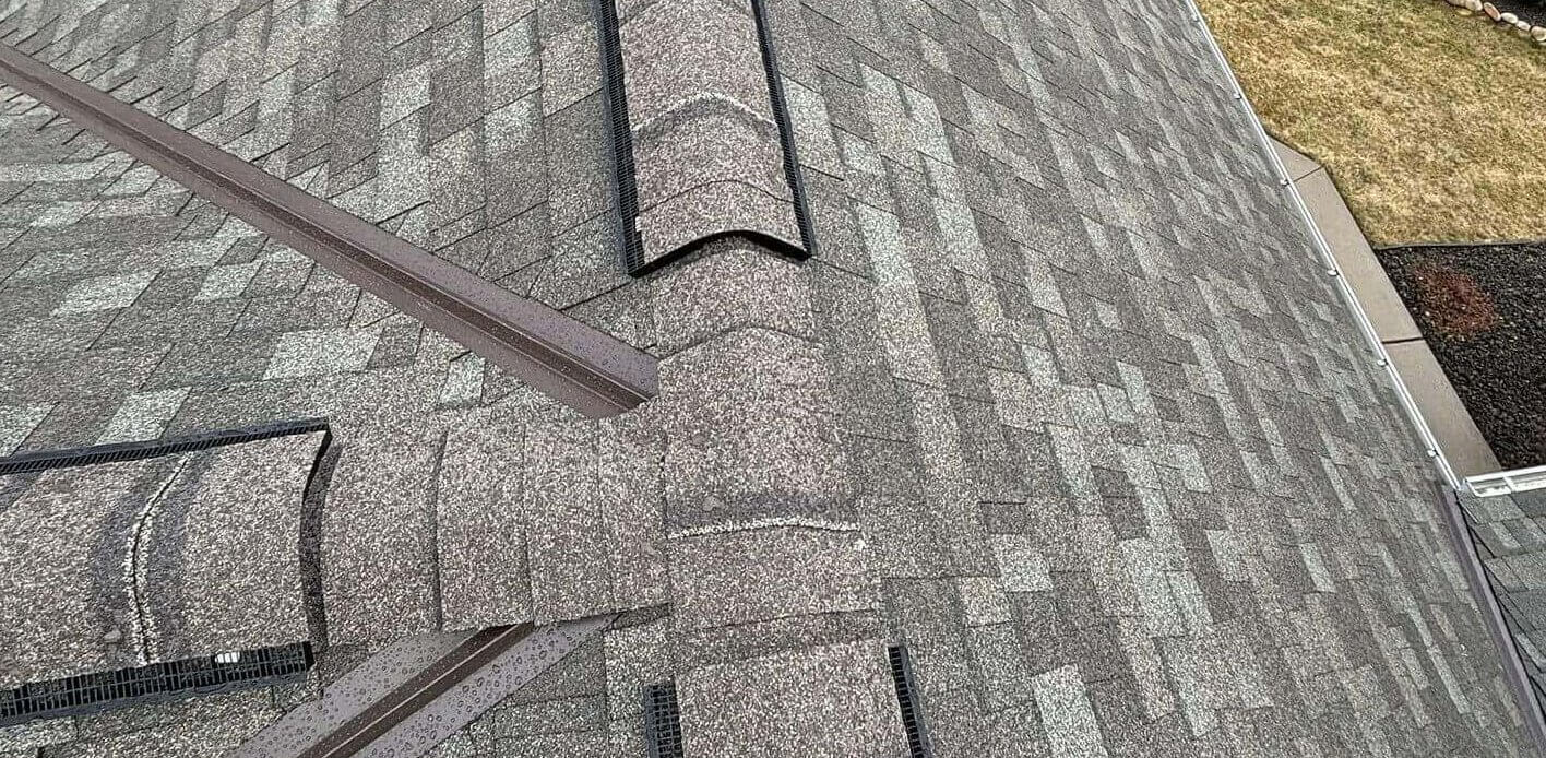 An overhead view of a recently installed shingle roof featuring a ridge cap ventilation system and intersecting hips.