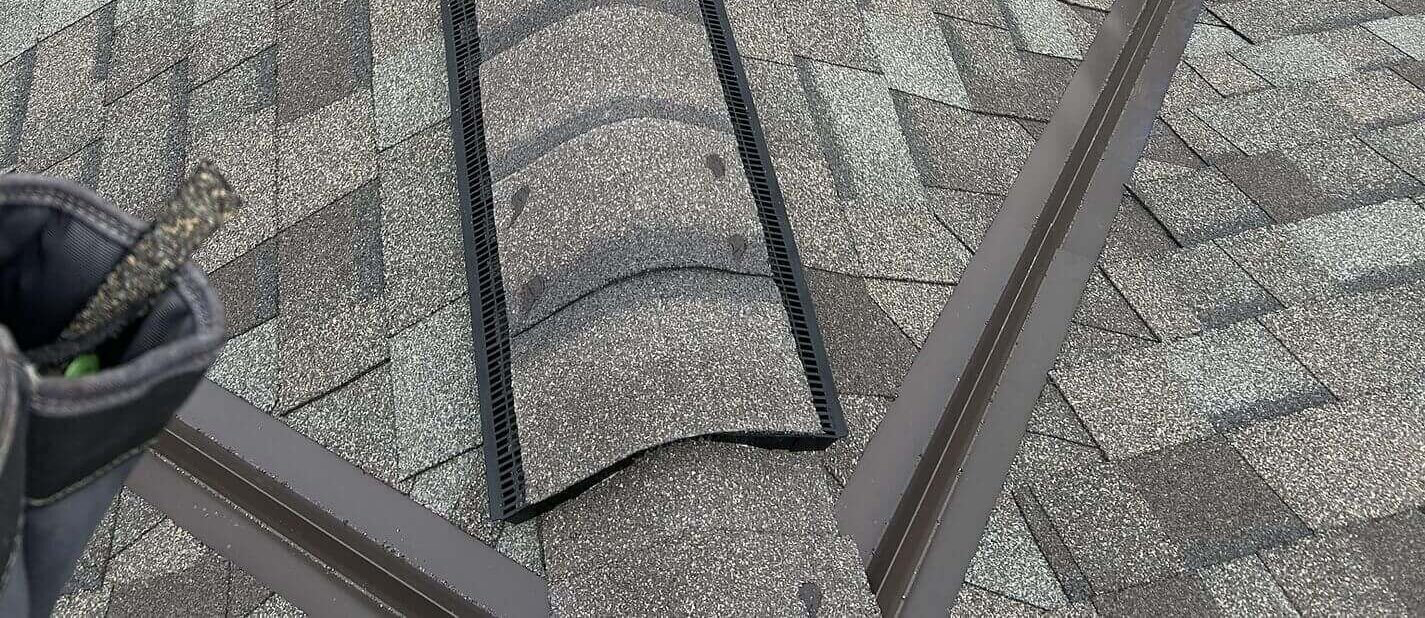 Gray shingle roof with two metal valleys that meet at the top and a continuous ridge vent.