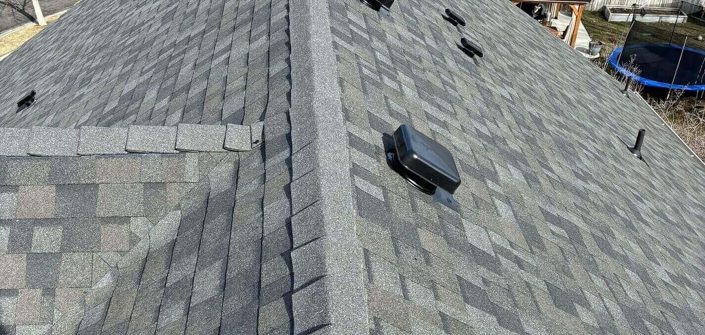A gray asphalt roof with a lot of ventilation boxes and a shingle pattern that stays the same down each slope.