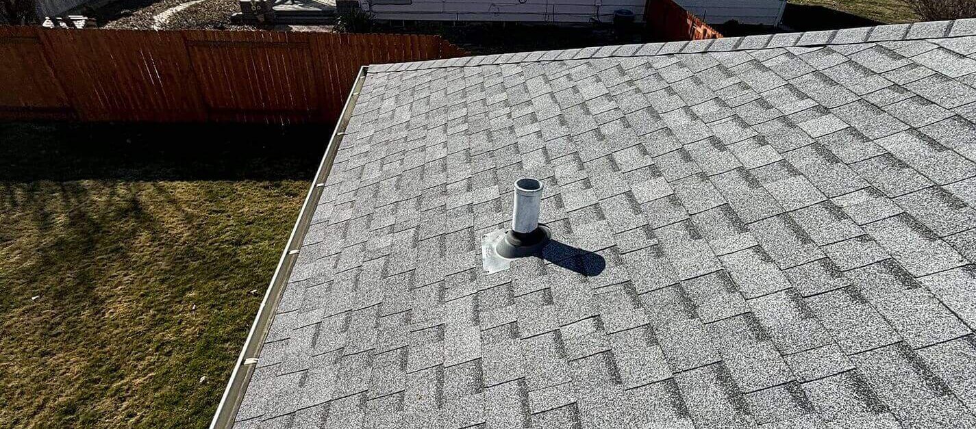 An overhead view of a gray architectural shingle roof with vents and a gutter system.