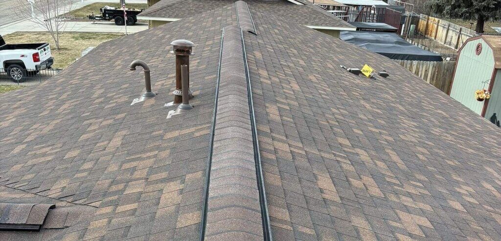 Brown shingle roof with a regular staggered pattern, sealed pipe penetrations, and a continuous ridge vent.