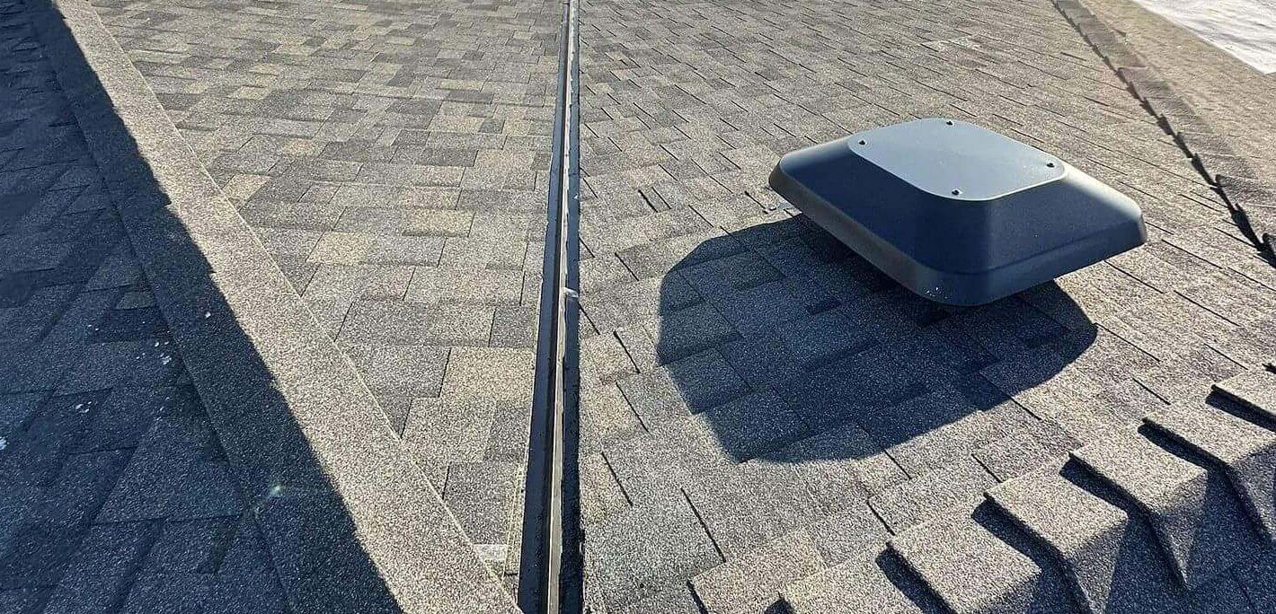 A rooftop view displays a neat shingle layout, box vent, and valley metalwork. (