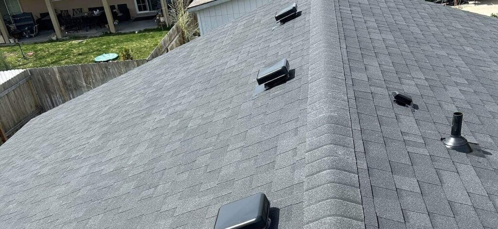 Box vents and pipe flashings are positioned uniformly across both slopes of the gray asphalt shingle roof with ridge cap.