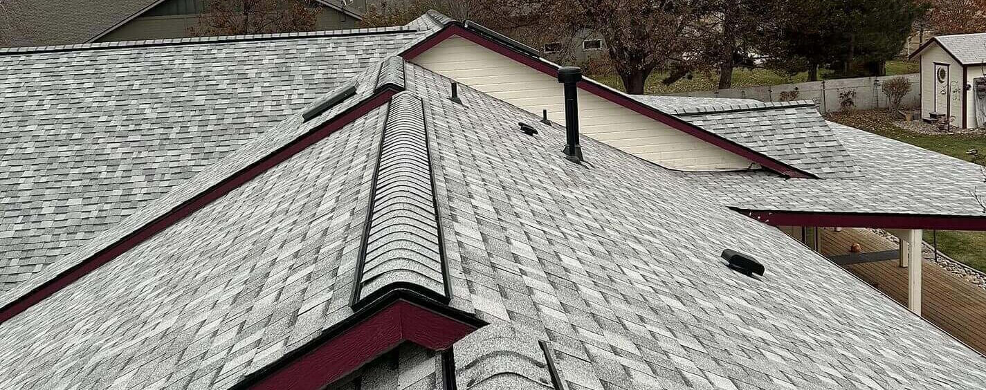 Architectural roof featuring bold red trim along fascia and transitions, black ridge caps, and light gray shingles.