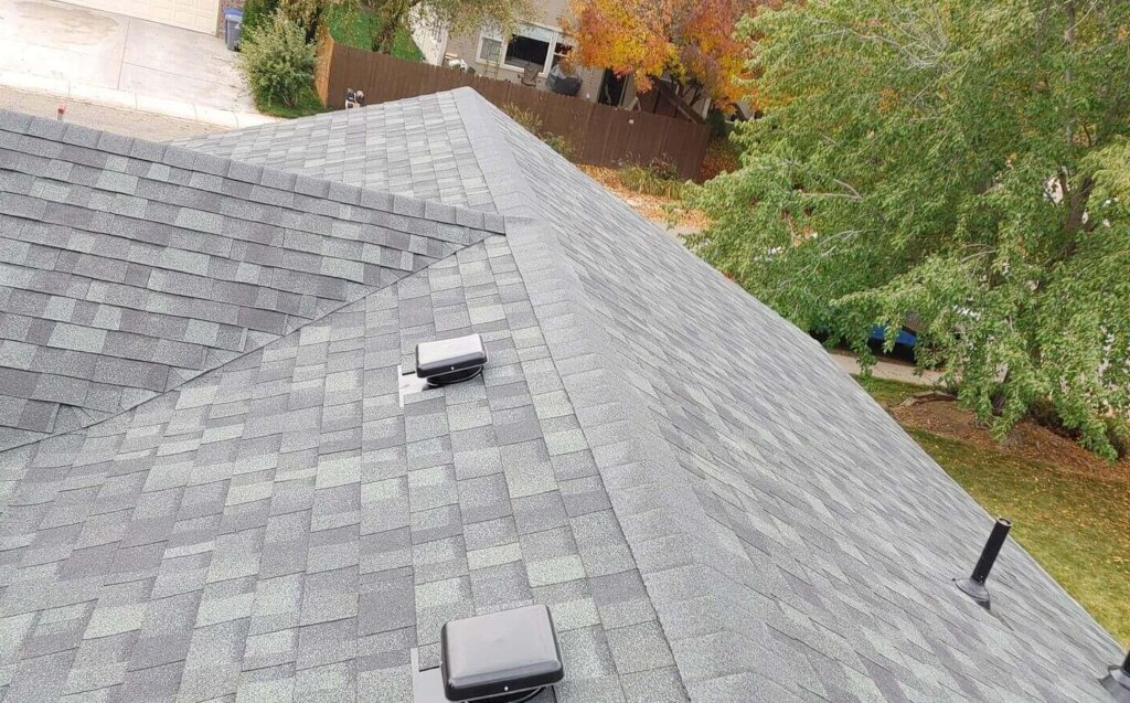 Recently placed shingle roof with tidy pipe flashing, exact ridge lines, and several attic ventilation boxes.