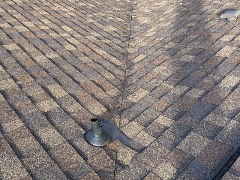 Roof valley with brown dimensional shingles meeting at center line, with plumbing vent flashing visible.