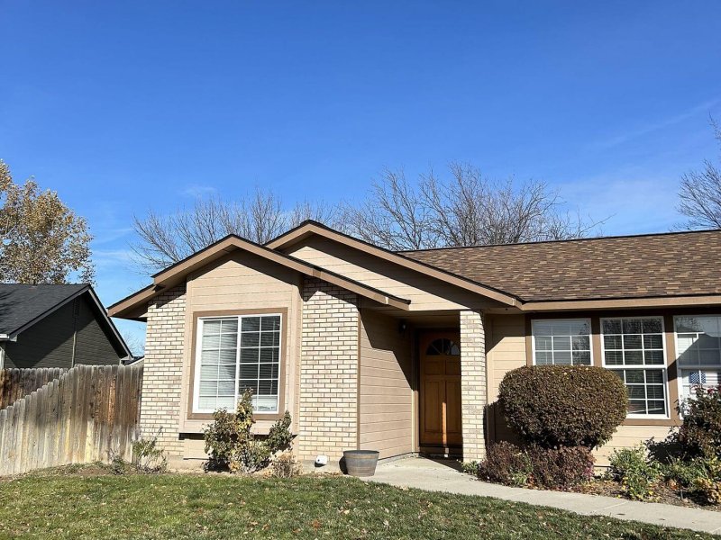 Brick and tan single-story home with new brown shingle roof against clear blue sky, front yard view.