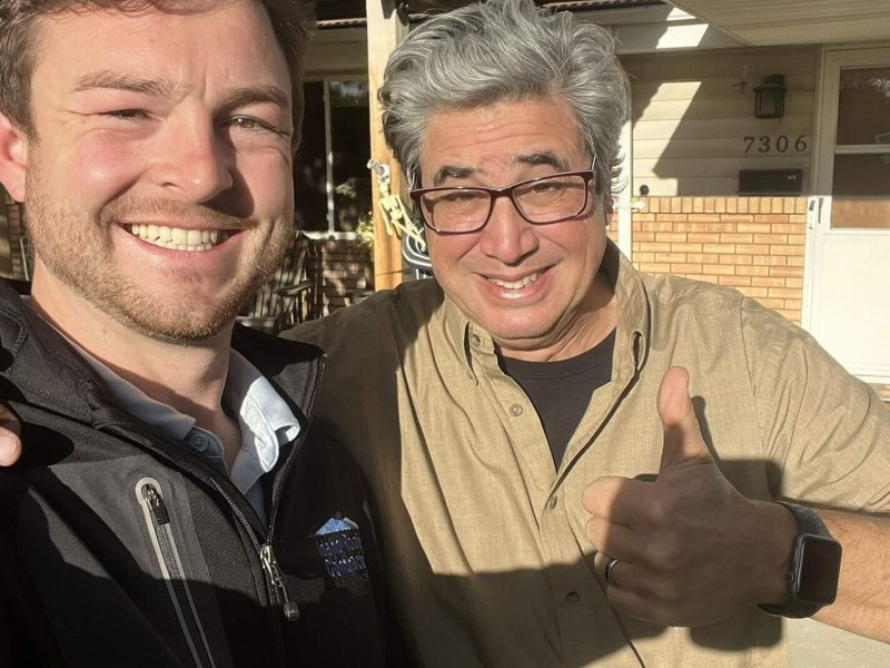 Roofing professional and enthusiastic customer giving thumbs up outside home on sunny day.