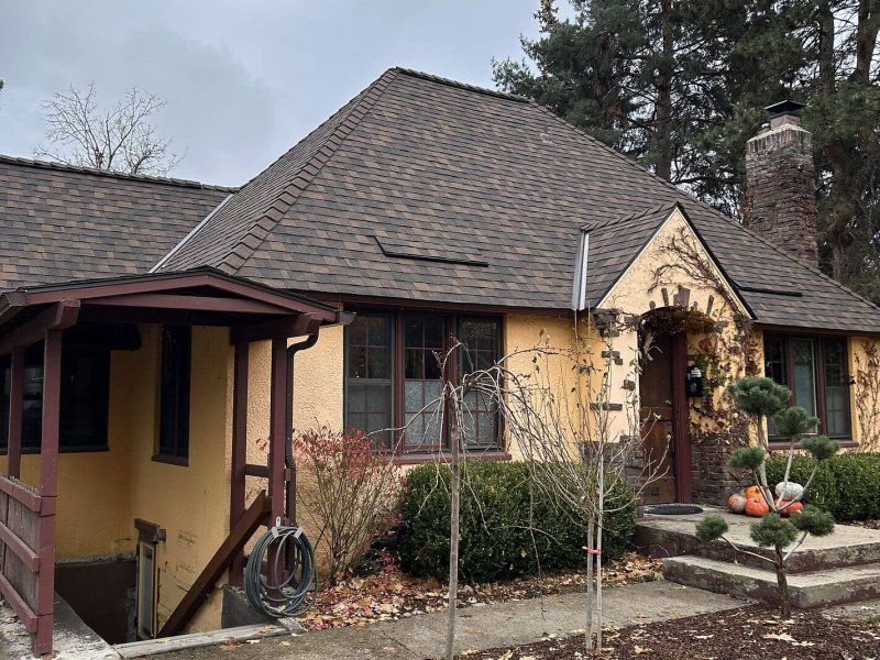 Multicolored roof shingles on Tudor-style yellow stucco house.