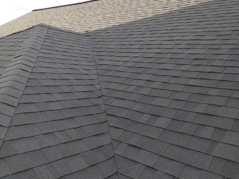 Charcoal gray roof shingles meeting at a steep valley intersection.
