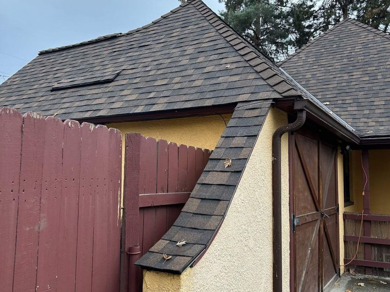 Side view of yellow stucco garage with steep gray dimensional shingle roof and wooden barn-style doors.