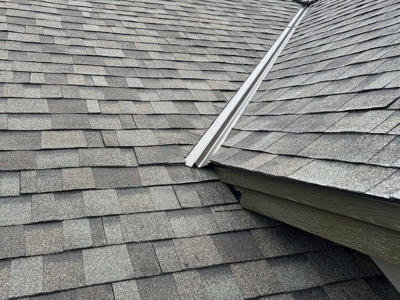 Asphalt shingle roof with white metal skylight flashing connecting different roof planes.
