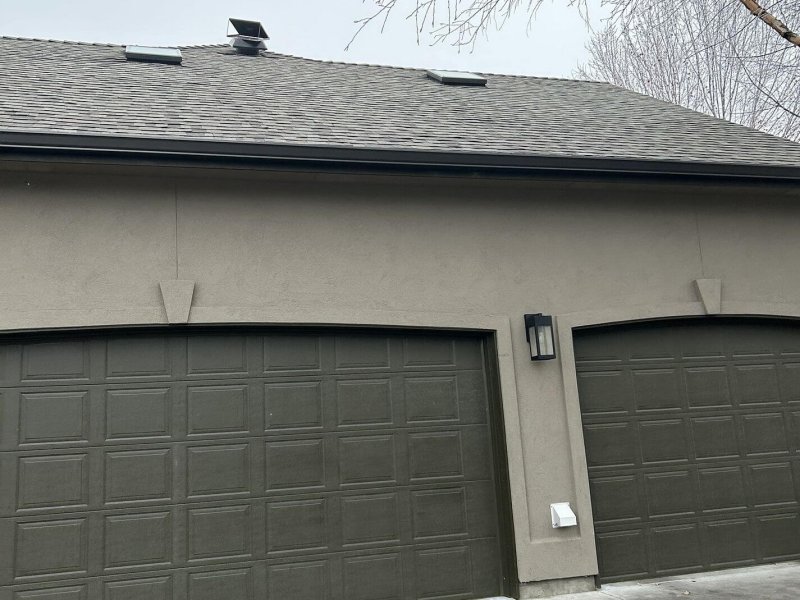 Solar roof vent on gray shingle roofing above garage doors.