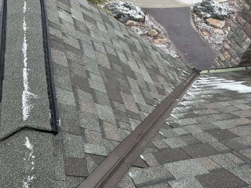 Roof valley with brown metal flashing properly installed between two sections of gray asphalt shingles.