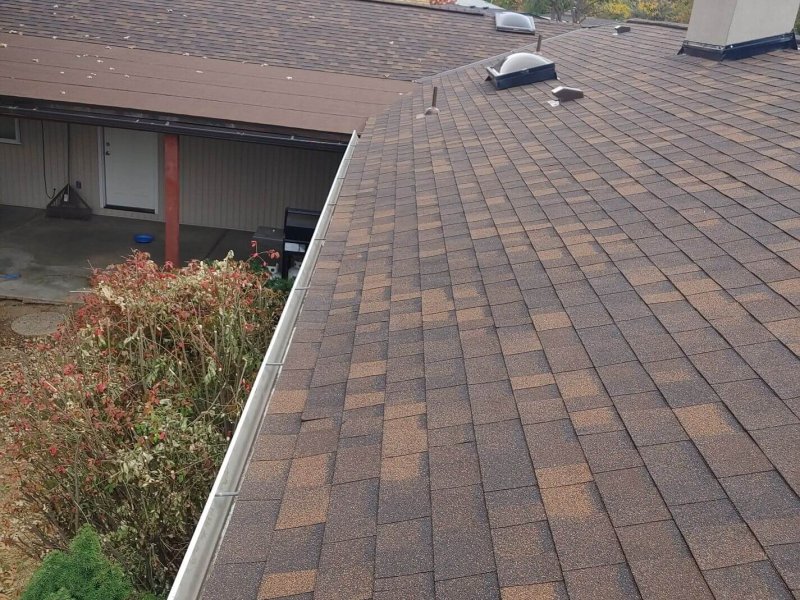 Brown dimensional shingles with multi-toned pattern, roof vents, and seamless gutter installation.
